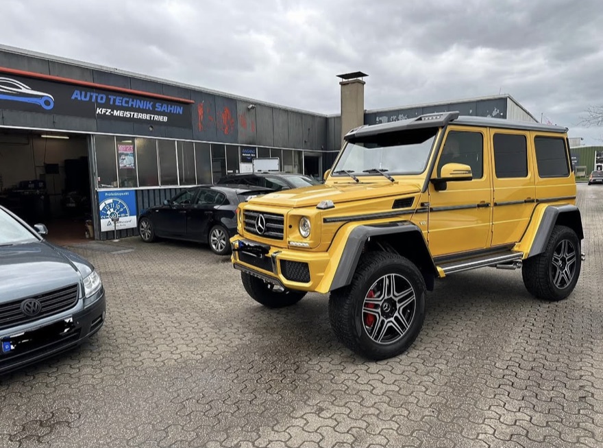Außenansicht von Auto Technik Sahin in Kamp-Lintfort: ein gelber Mercedes G-Klasse steht vor dem Betrieb mit dem Firmenschild „Auto Technik Sahin – KfZ-Meisterbetrieb“.
